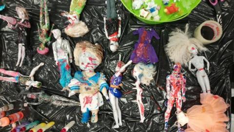 various toy dolls covered with paint and with distressed hair and clothes made to look like zombies