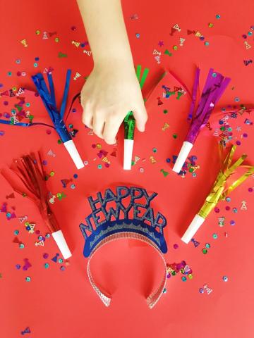 five foil noisemaker horns surrounding a crown that says "happy new year". a hand reaches for a noisemaker