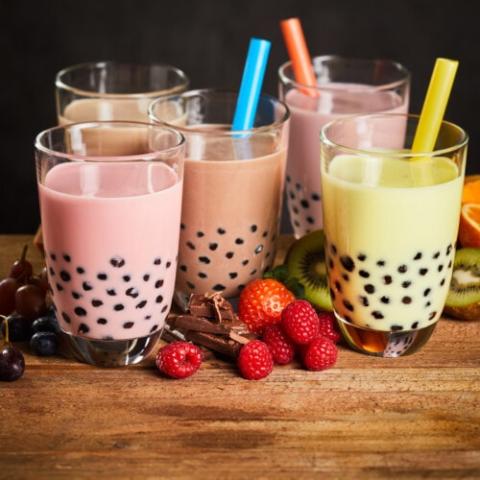 five glasses of bubble tea in different colors and flavors on a table surrounded by berries and chocoalte