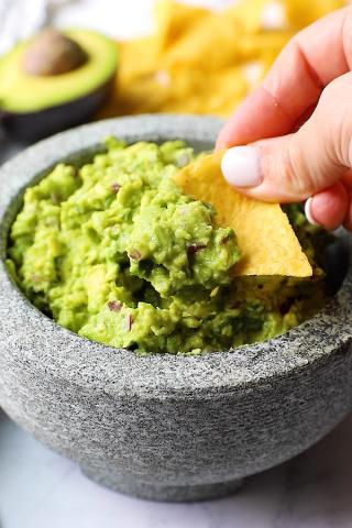 A hand holding a chip dips into a bowl of guacamole 
