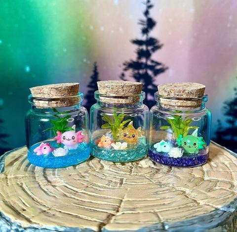 three small glass bottles with axolotl figurines and decorations inside