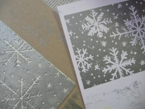 Piece of foam with snowflakes carved into it, sits next to a piece of paper with the same design which is made using printmaking techniques