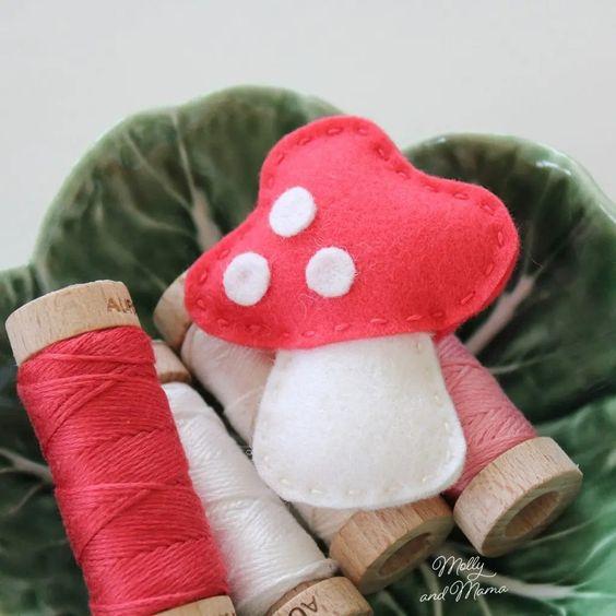 felt mushroom with a red cap and white spots sitting atop four spools of thread