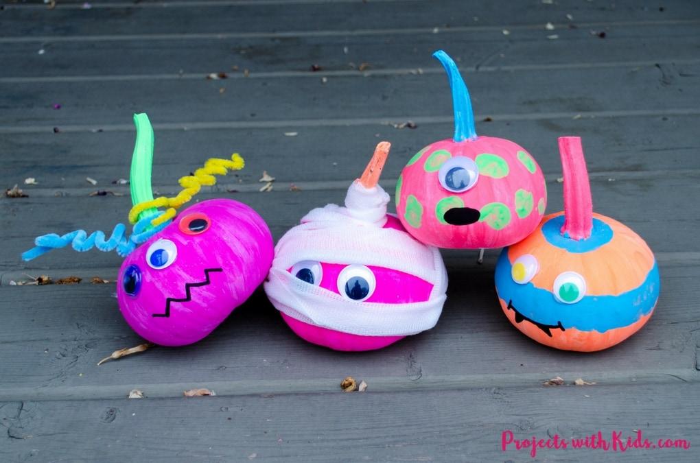 four small pumpkins decorated with neon paint, googly eyes, pipe cleaners and other assorted craft supplies