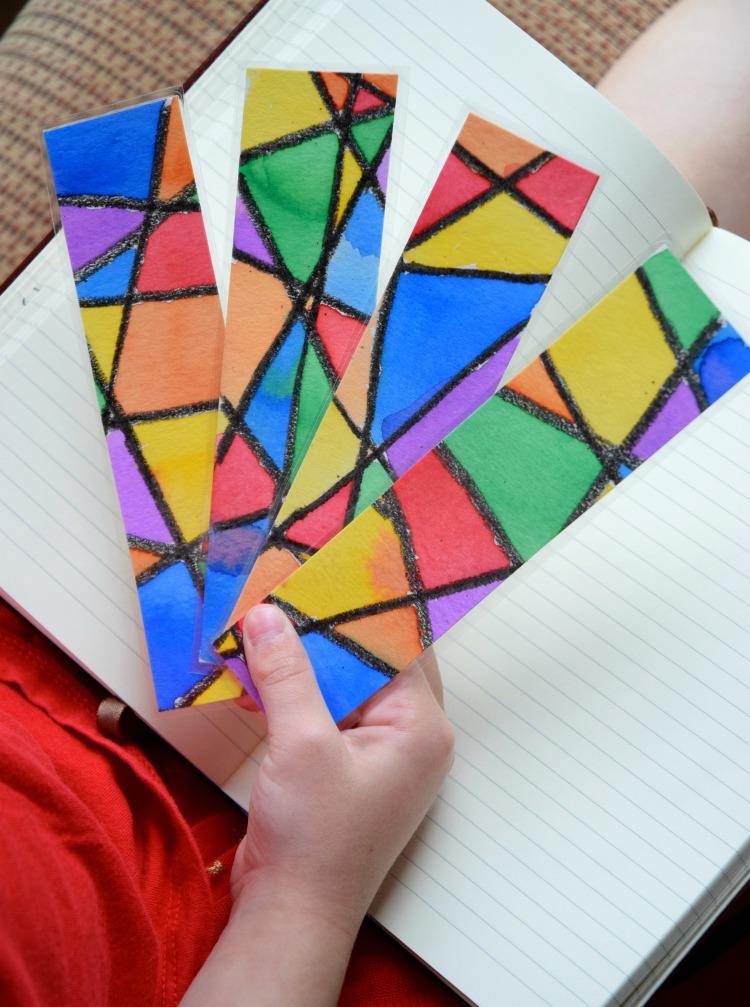 hand holding four bookmarks with colorful abstract stained glass-like patterns