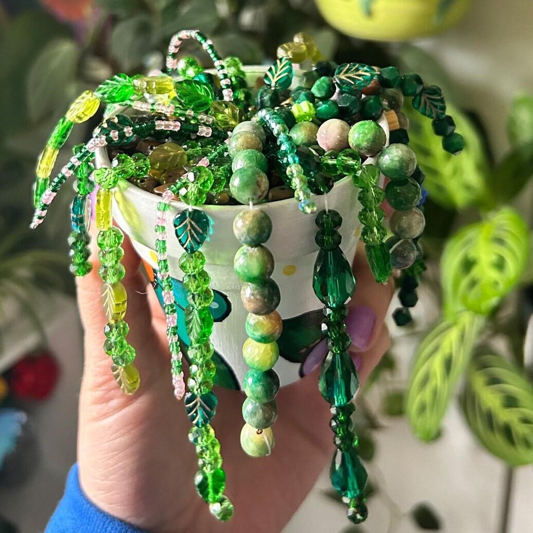 hand holding a vining plant made of different shades and shapes of green beads